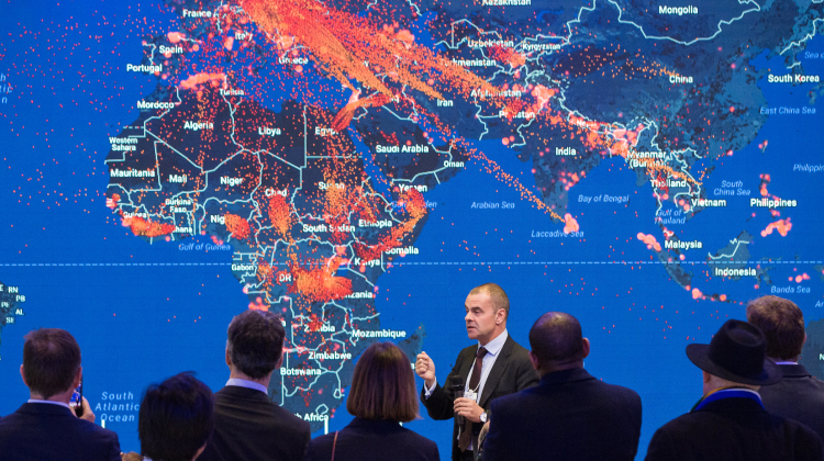 A man speaking in front of a map of the world