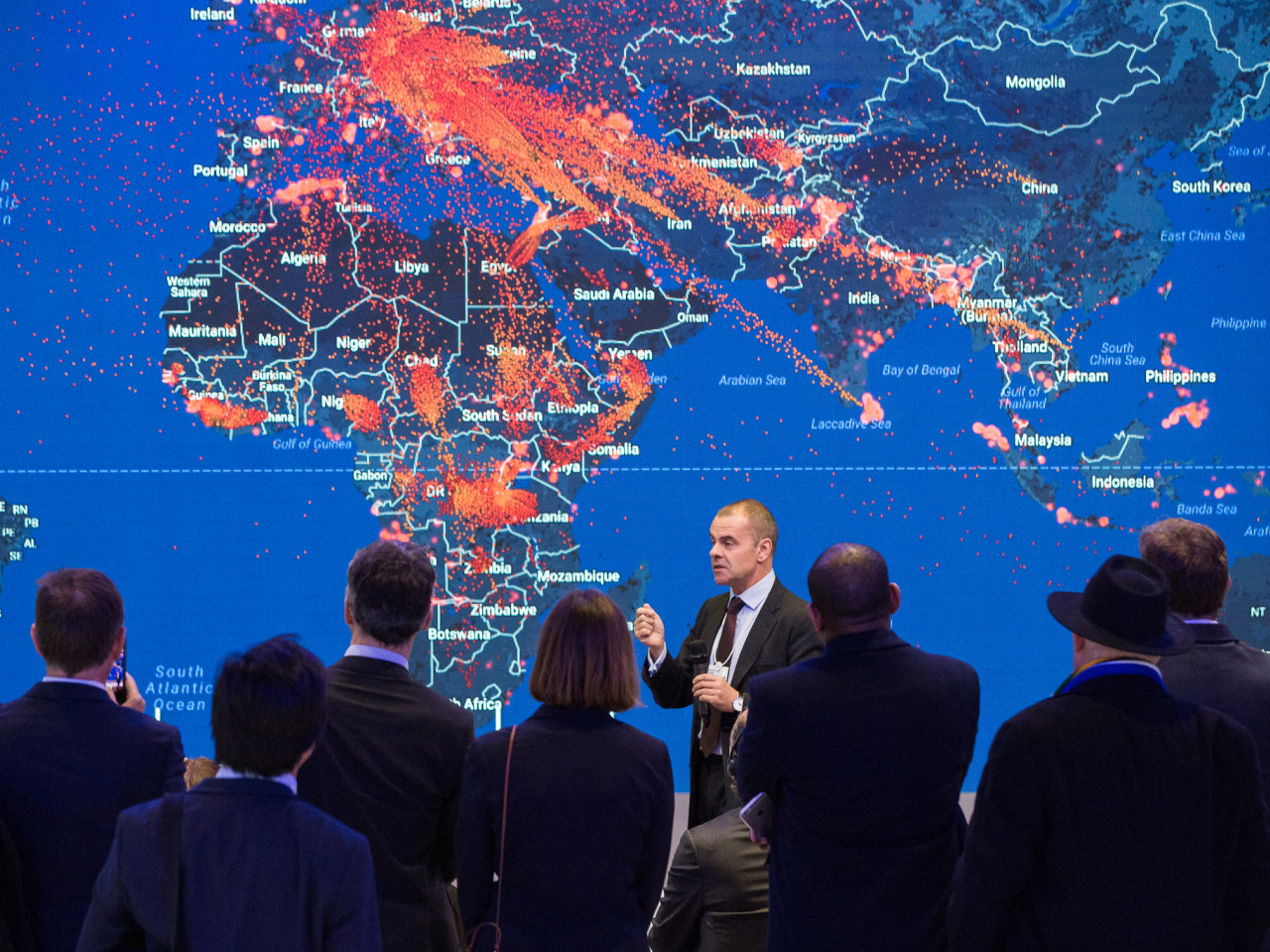 A man speaking in front of a map of the world